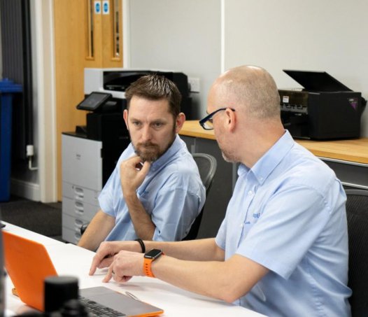 two men talking at desk